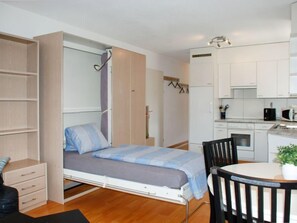 A compact room with a bed, a small kitchenette, a dining area, and a wardrobe.