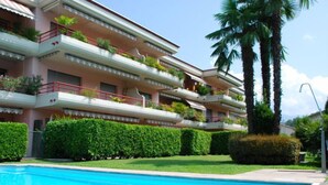 Un hotel de varios pisos con piscina, balcones con plantas y palmeras.