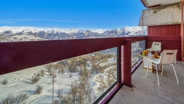 A balcony with a view of snow-covered mountains and a dining area with chairs and a table. - Lunik Orion by Interhome (Le Corbier)