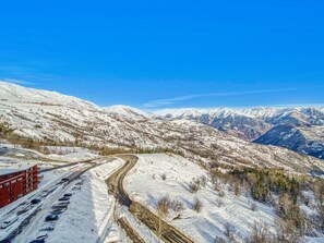 Un paysage montagneux enneigé, avec une route sinueuse et un bâtiment rouge sur la gauche.