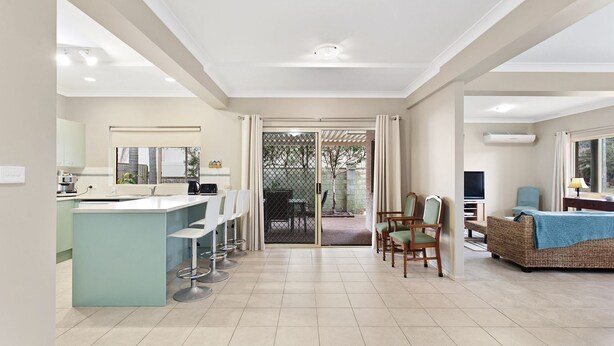 A modern kitchen with a bar area, a dining area with chairs, and a living room with a TV and seating. - Position, space and privacy (Nelson Bay)