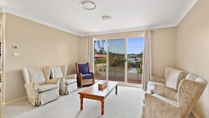 A spacious living room with a large sliding glass door leading to a balcony. There are two patterned armchairs, a wooden coffee table, and a blue chair. - Position, space and privacy (Nelson Bay)
