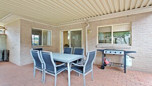 Une terrasse extérieure avec une table et des chaises en métal, un barbecue et un mur en briques.
