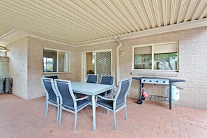 An outdoor patio with a metal table and chairs, a grill, and a brick wall. - Ajax Avenue, 6 (Nelson Bay)