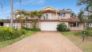 A two-story house with a brick exterior, a front garage, and a paved driveway. - Position, space and privacy (Nelson Bay)