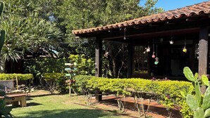 A garden with a patio area, a cactus, and a building with a tiled roof. - Numa Boa Hostel (Búzios)