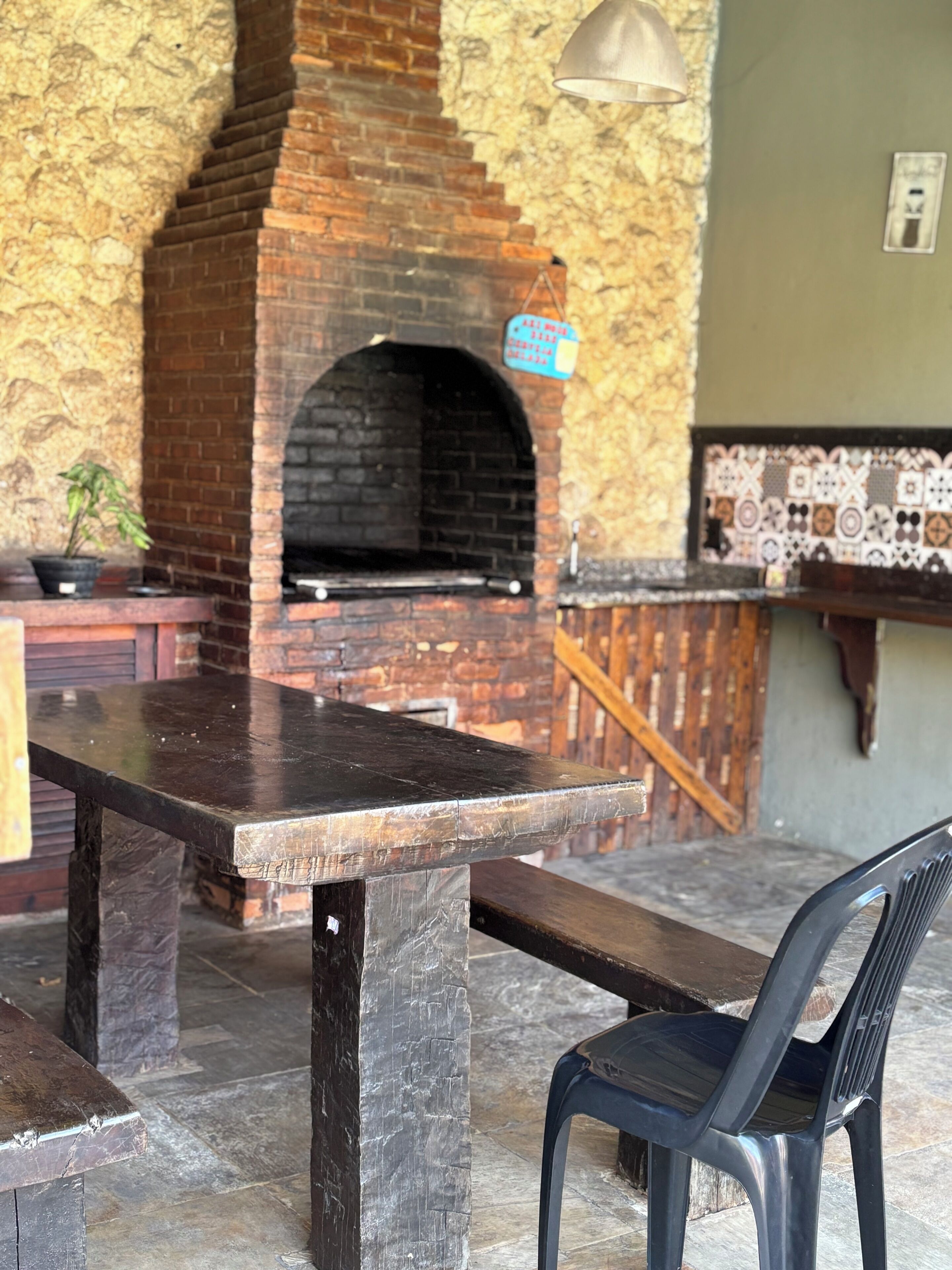 Un horno de ladrillo al aire libre, con un fondo de pared de piedra, una mesa de madera y una silla de plástico.