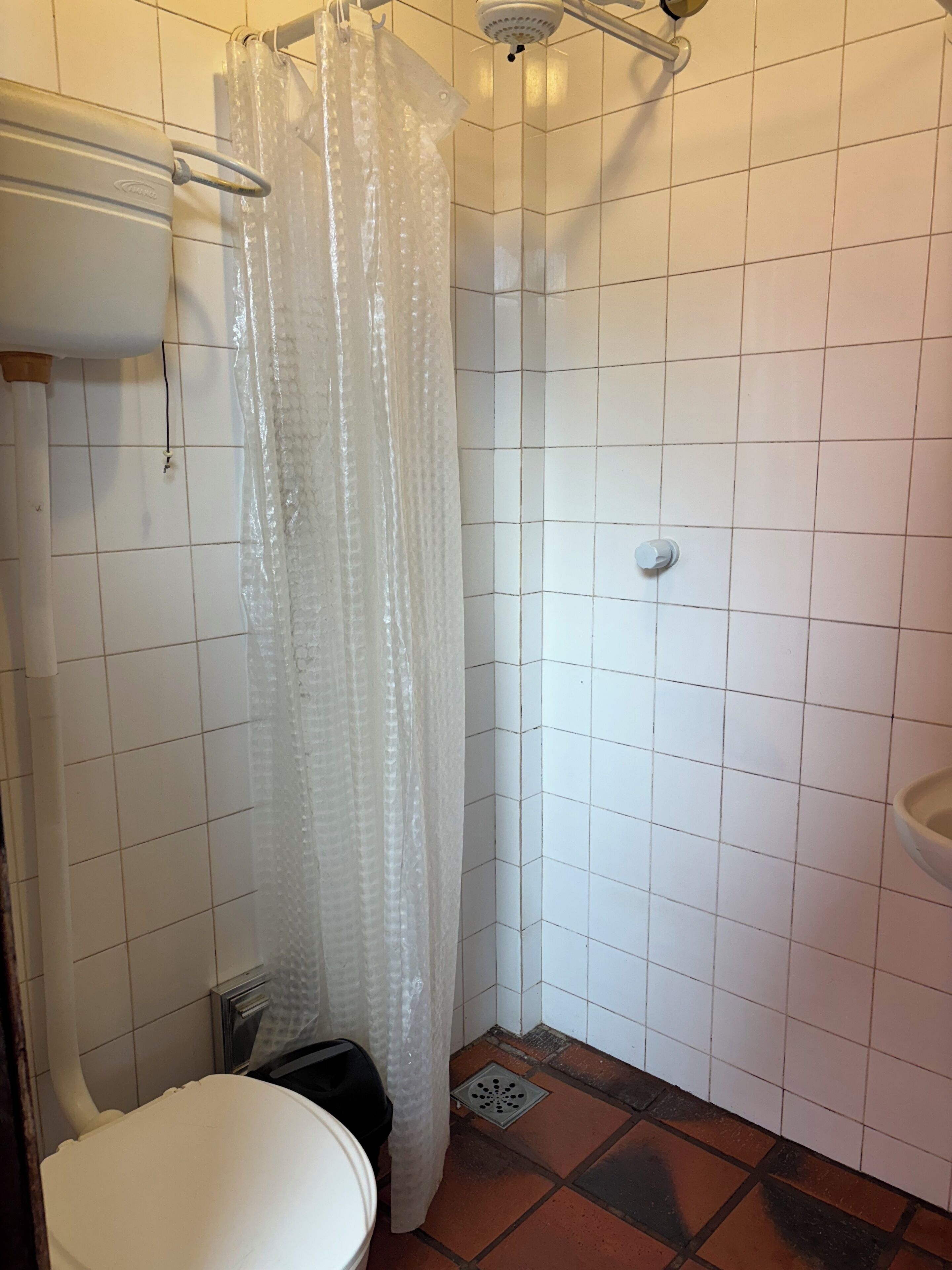 Un baño pequeño con azulejos, cortina de ducha, inodoro y lavamanos.