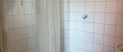 Un baño pequeño con azulejos, cortina de ducha, inodoro y lavamanos.