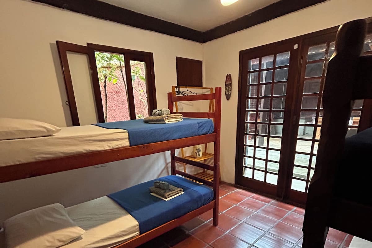 A room with two bunk beds, a ceiling fan, a window with a view, and a door with glass panels.