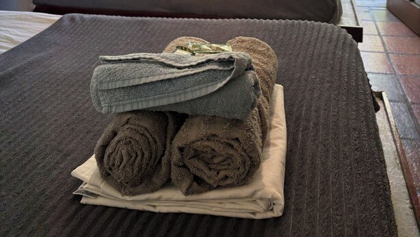 A hotel room with two beds, a view of the garden through an open door, and a stack of towels on the bed. - Numa Boa Hostel (Búzios)