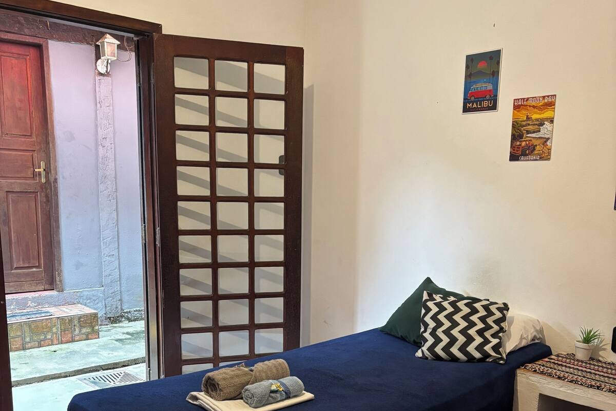 A bedroom with a bed, a nightstand, and a window with a view of the street.
