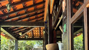 An outdoor seating area with wooden tables and benches, a covered roof, and a view of the surrounding greenery. - Numa Boa Hostel (Búzios)