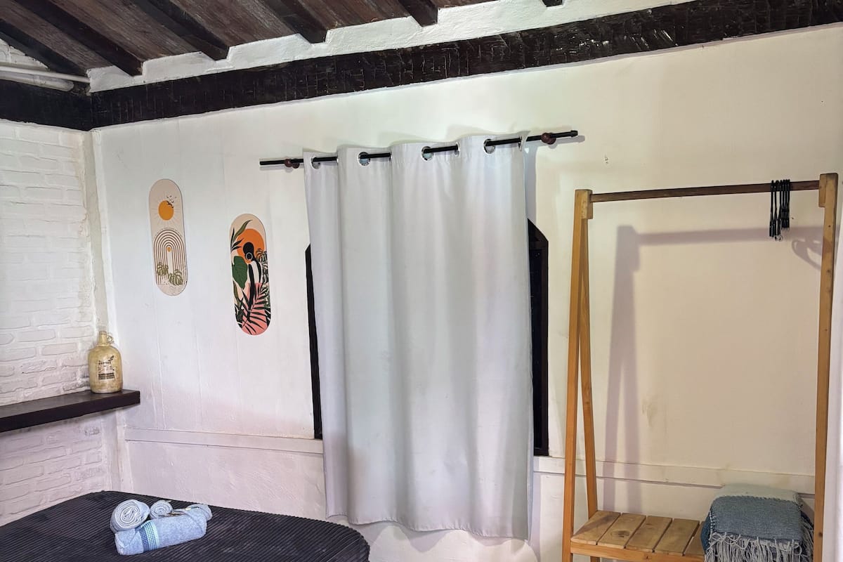 A room with a bed, a wooden bench, a hanging chair, a curtain, and a wall with artwork.