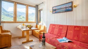 A cozy room with a wooden table, a red sofa, and a painting of a mountain landscape. - Arcelle 505 by Interhome (Val Thorens)