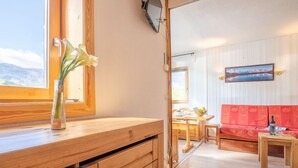 A wooden interior with a dining area, a sofa, and a window with a view of mountains. - Arcelle 505 by Interhome (Val Thorens)