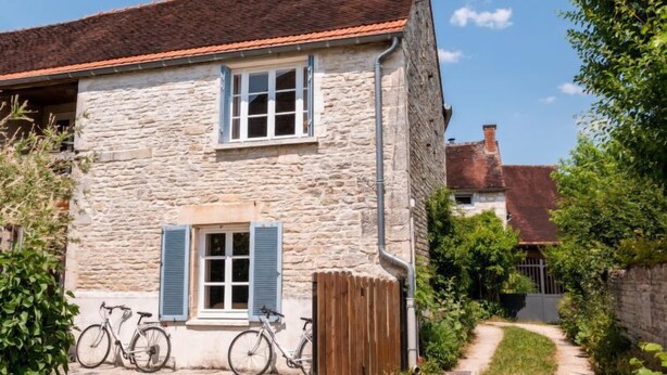Un bâtiment en pierre avec un toit recouvert de tuiles rouges, une porte en bois et deux vélos garés devant.