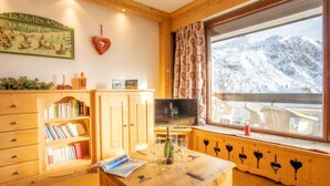 Habitació acollidora amb mobles de fusta, una prestatgeria, un televisor de pantalla plana i una finestra amb vista a una muntanya nevada.
