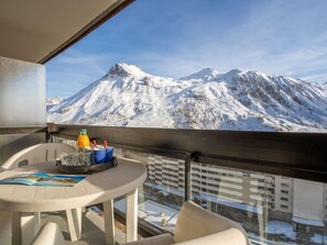 Un balcón con una mesa, un vaso de jugo de naranja y un vaso. El balcón tiene vista a una montaña nevada.