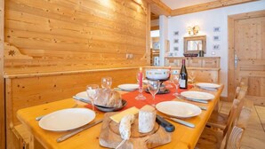 Taula de dinar de fusta preparada per a un àpat, amb plats, coberts, una barra de pa, una taula de formatge i una ampolla de vi.