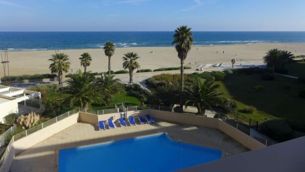 A pool area with lounge chairs, palm trees, and a view of the beach and ocean.