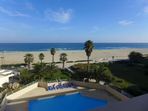A pool area with lounge chairs, palm trees, and a view of the beach and ocean. - Copacabana by Interhome (Canet-Plage)