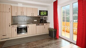 A compact kitchen with wooden cabinets, a microwave, a stove, and a television on a shelf. - Pfeifer by Interhome (Pians)