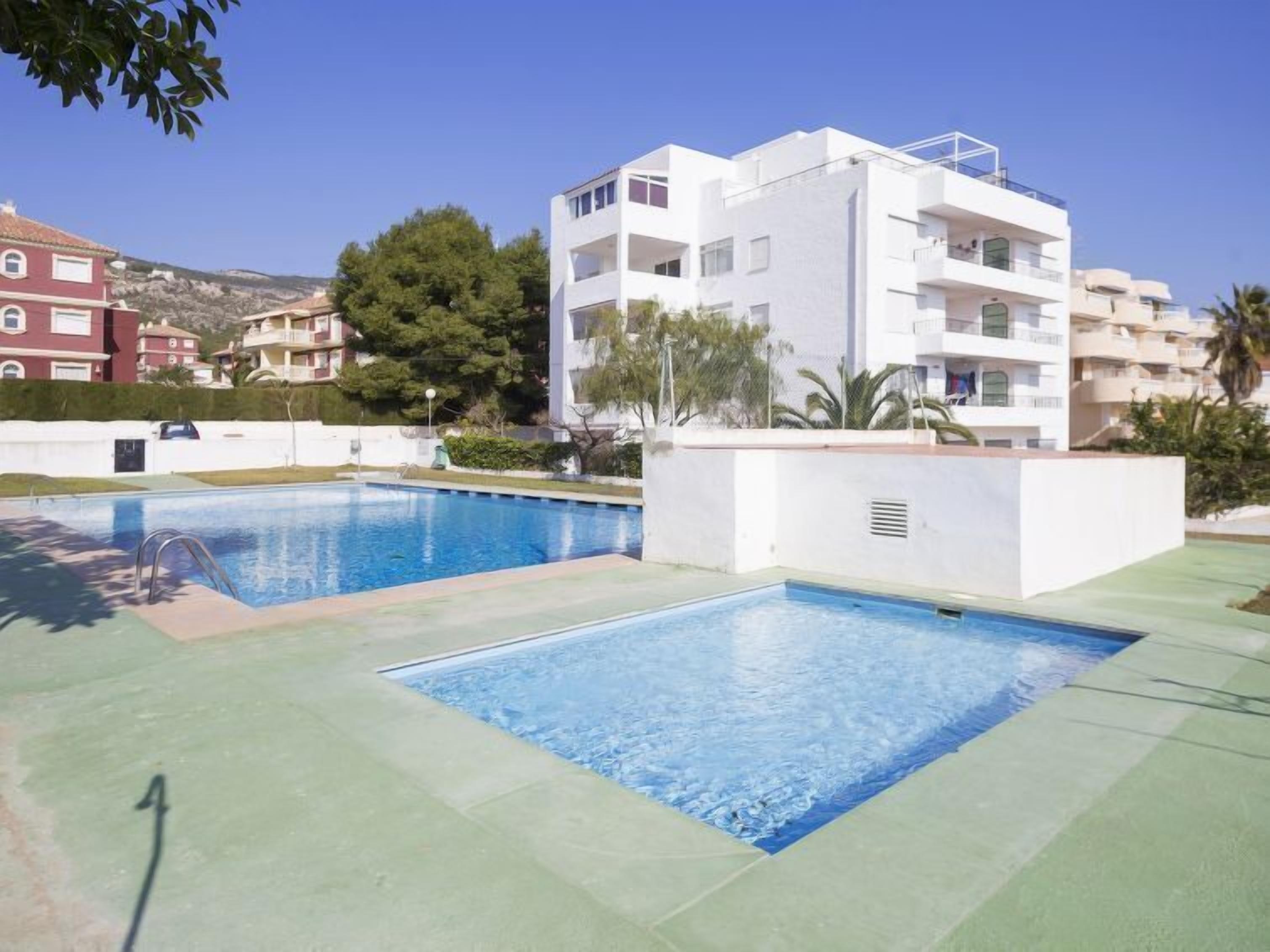 A swimming pool area with two pools, surrounded by a white building with balconies.