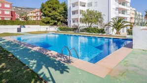 Una piscina con agua cristalina azul, rodeada de césped y un edificio blanco con balcones.