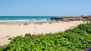 Una playa con sombrillas, cabañas y acantilados rocosos.