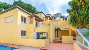 Un edificio amarillo de dos pisos con piscina, un área exterior cubierta y una escalera que conduce al piso superior.