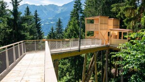 Una terraza de madera con barandilla de metal que da vista a un área boscosa y montañas al fondo.