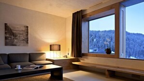 Una sala de estar moderna con un sofá, una mesa de centro, una lámpara y un ventanal con vistas a un bosque nevado.