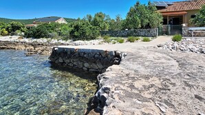 Eine Küstenlandschaft mit klarem Wasser, felsigem Ufer, einer Steinmauer und einem Gebäude mit einem Ziegeldach.