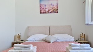 Ein Doppelbett mit einer rosafarbenen Steude, zwei weißen Kissen und zwei Nachttischen mit Lampen.