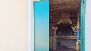 Ein offenes Durchgang zu einem Außenbereich mit Steinküche, der ein Backofen, ein Betonboden und eine Holzbalkendecke aufweist.