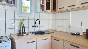 Eine Küche mit einem Gasherd, einem Spülbecken mit Wasserhahn, Schränken und einem Fenster.