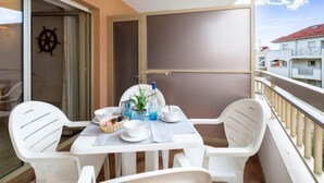 Een balkon met een tafel gedekt voor twee personen, witte plastic stoelen en een uitzicht op gebouwen.