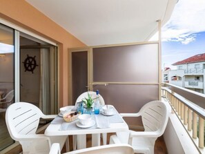 A balcony with a table set for two, white plastic chairs, and a view of buildings in the background. - Les Platanes by Interhome (Sainte Maxime)