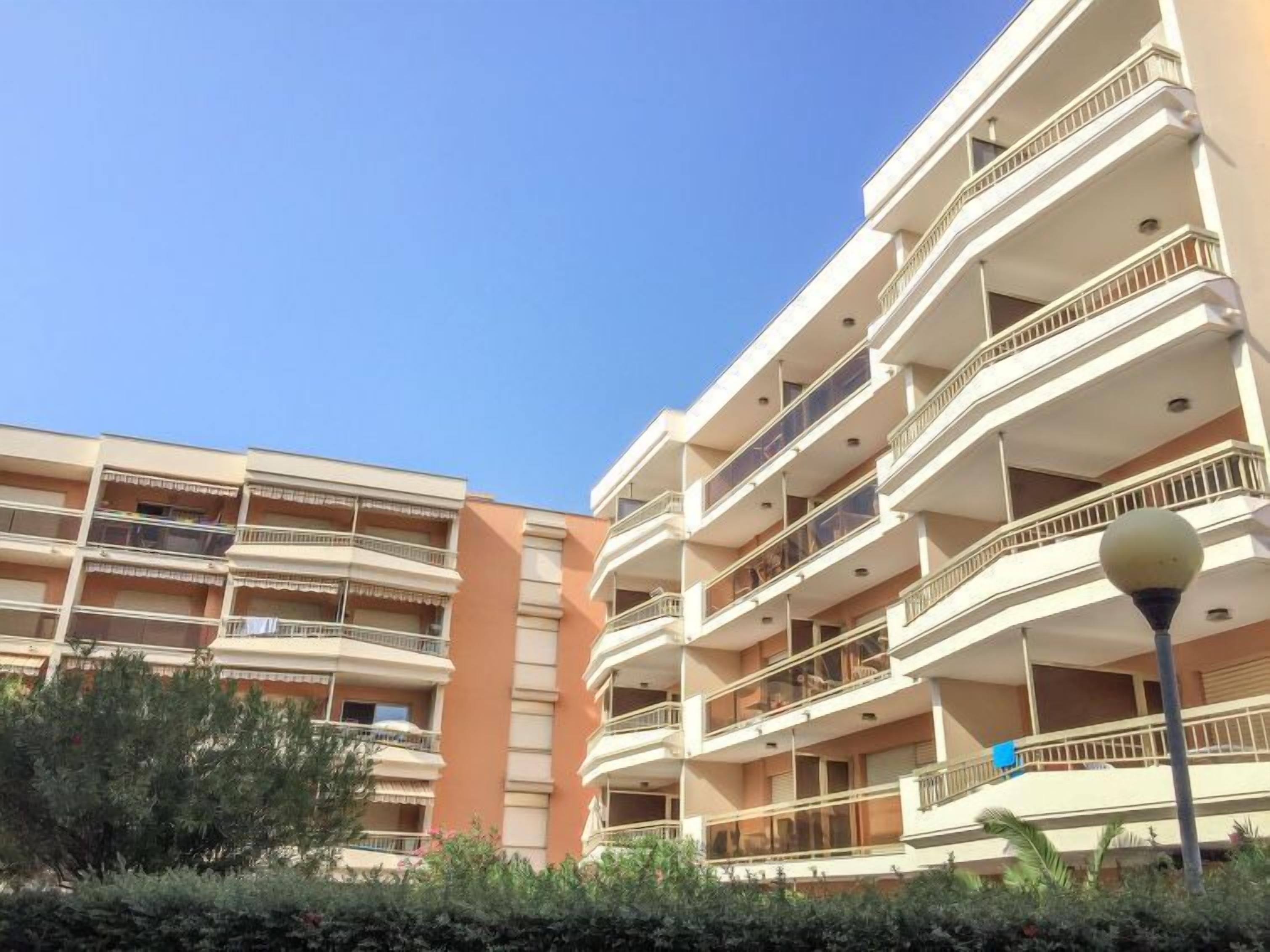 A multi-story residential building with balconies, a street lamp, and a clear blue sky.