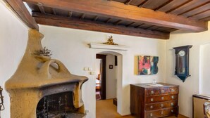 Een rustiek interieur met een stenen open haard, houten balken in het plafond, een houten dressoir en een klok aan de muur.
