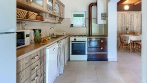 A compact kitchen with wooden cabinets, a microwave, a stove, and a washing machine. - Vacation home Ana by Interhome (Rovinj/Rovinjsko Selo)