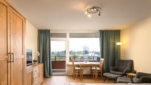 Hotellihuone, jossa on sänky, työpöytä tuoleineen, televisio ja parveke, jossa on verhot.