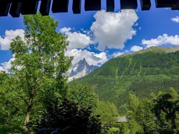 A mountain landscape with a prominent peak, lush green trees, and a small building in the foreground.