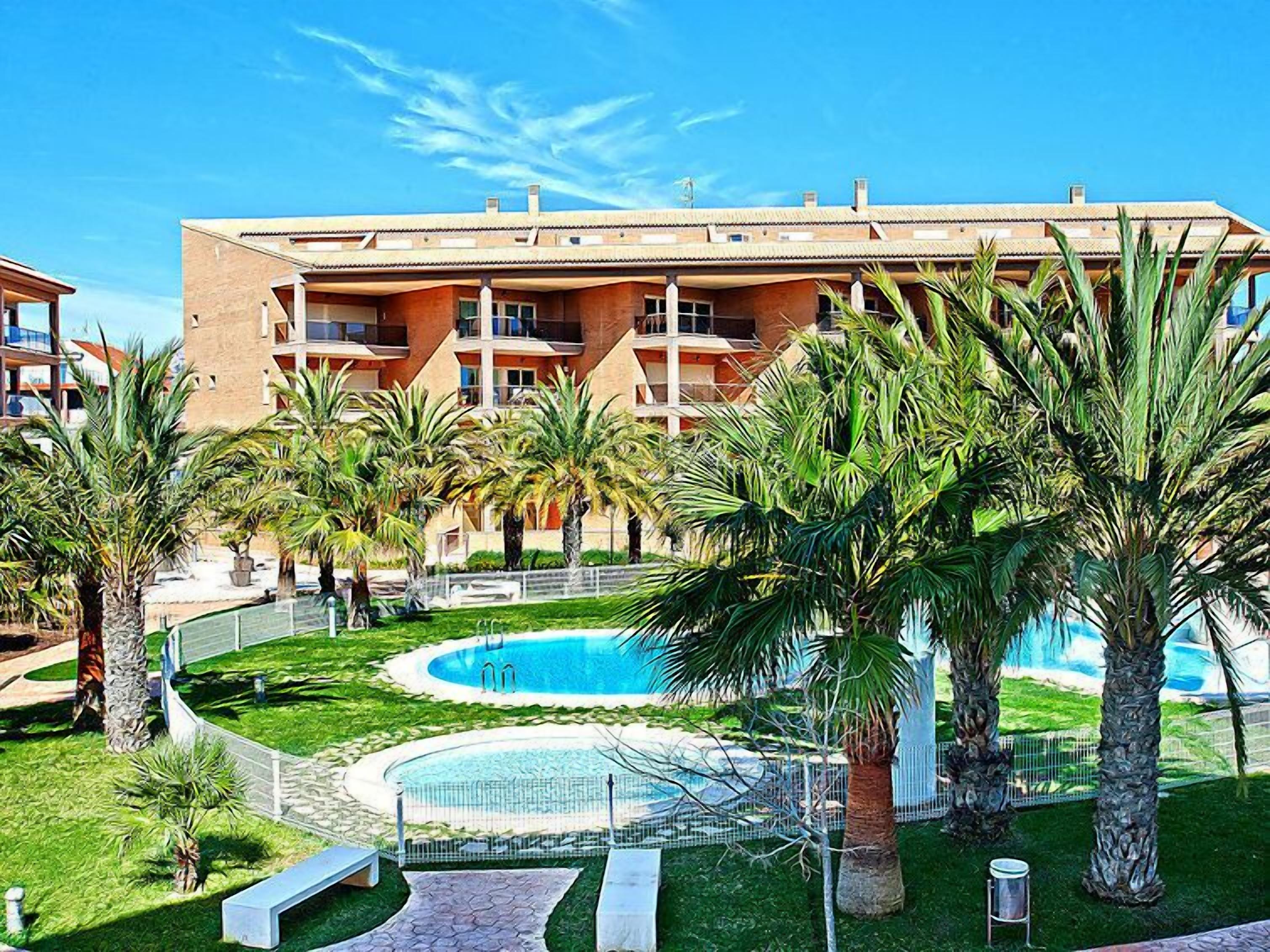 Un hôtel doté d’une piscine entourée de palmiers et d’une pelouse bien entretenue.