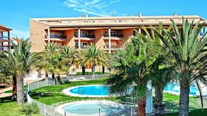 A hotel with a swimming pool surrounded by palm trees and a well-maintained lawn.