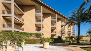 A multi-story hotel with balconies, a palm tree, and a gravel courtyard.