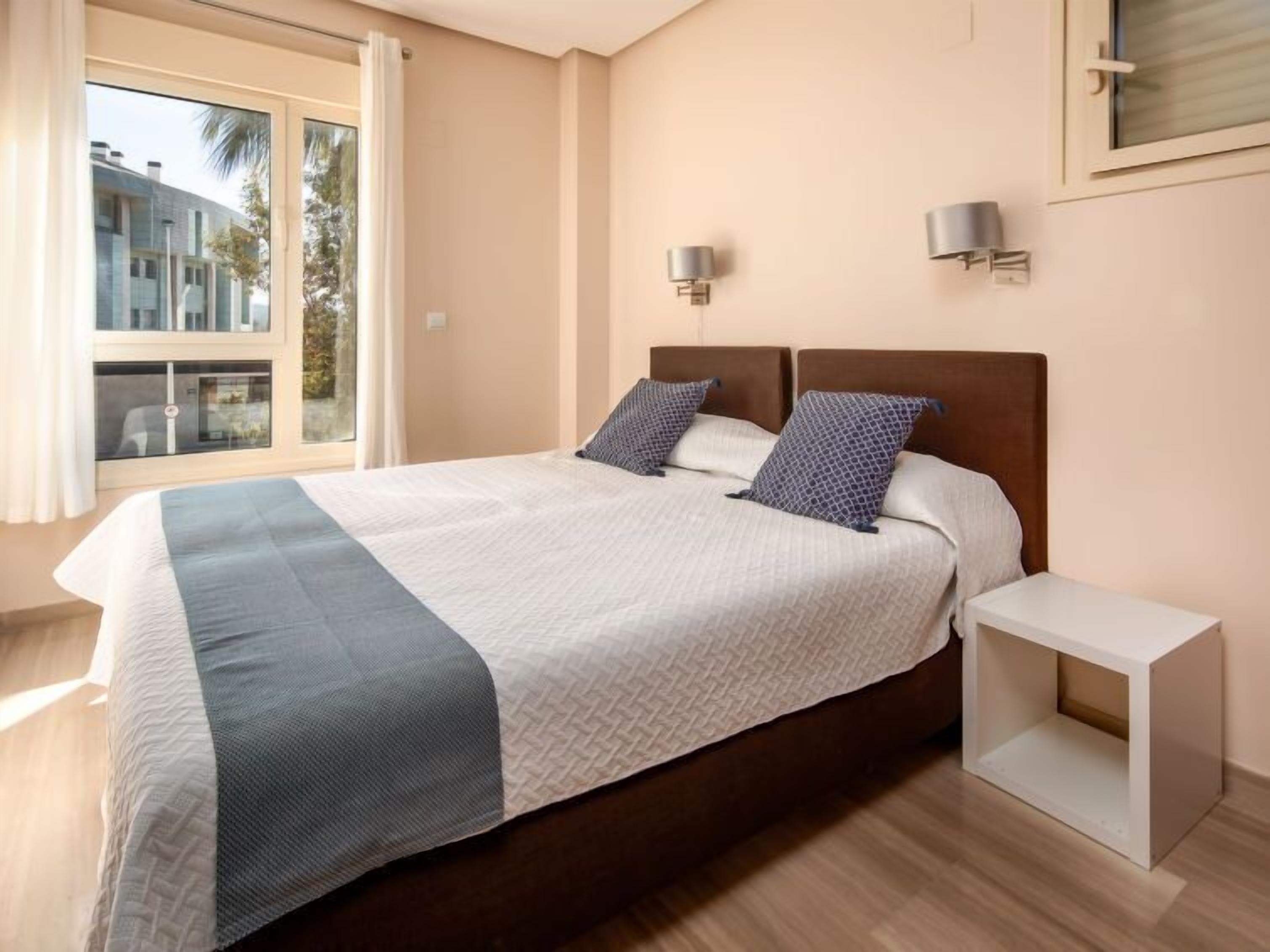 A modern bedroom with a large bed, two wall-mounted lamps, and a window with curtains.