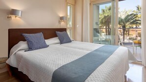 A large bed with a wooden headboard, two wall-mounted lamps, and a view of palm trees through a glass door.