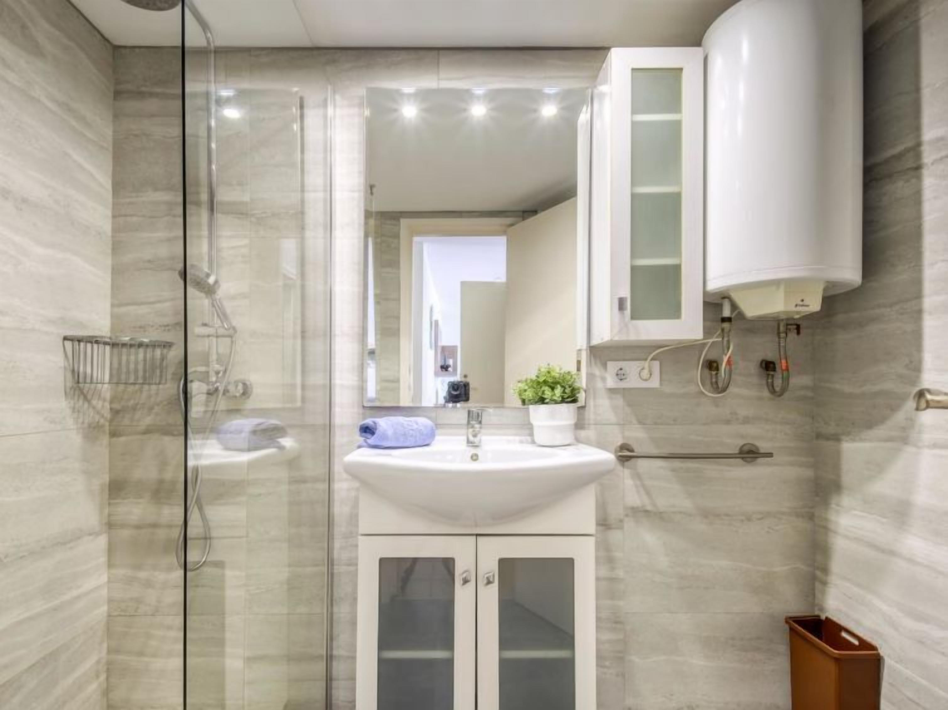 A modern bathroom with a glass-enclosed shower, a white sink, and a cabinet with glass doors.